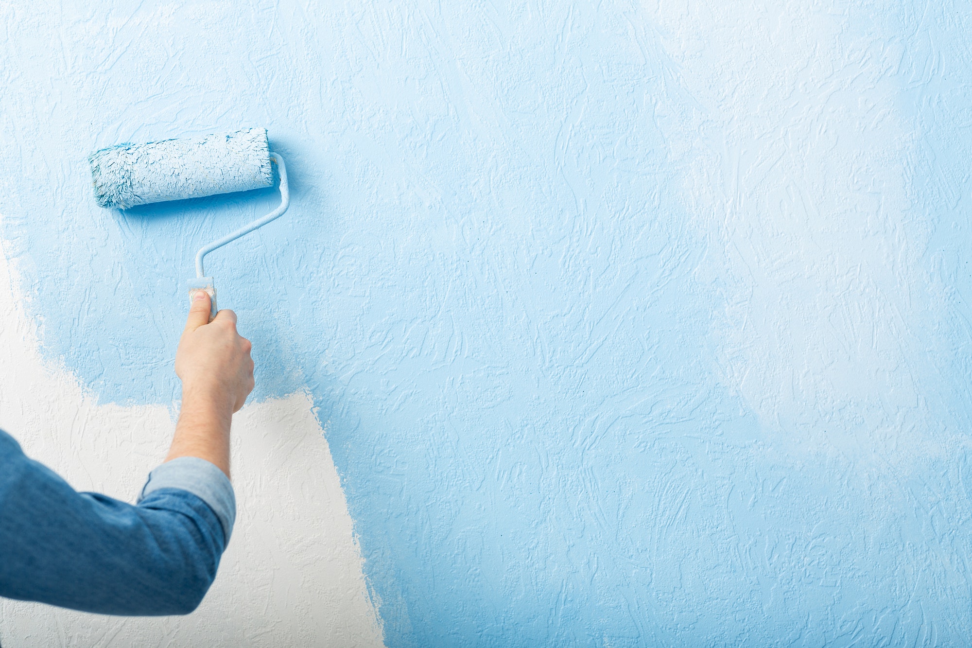 Paints texture wall with roller in blue